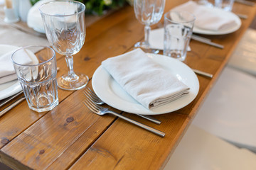 White napkin on a plate next to glasses, forks, knives, plates on a wooden table in the restaurant served for dinner. Set dining table in loft style