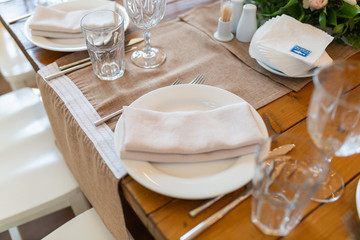 White napkin on a plate next to glasses, forks, knives, plates on a wooden table in the restaurant served for dinner. Set dining table in loft style