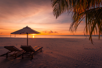 Beautiful tropical sunset scenery, two sun beds, loungers, umbrella under palm tree. White sand, sea view with horizon, colorful twilight sky, calmness and relaxation. Inspirational beach resort hotel