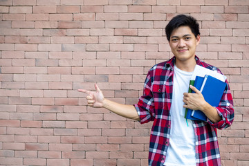 Asian male students wear plaid shirts. Standing next to a brick wall, carrying books, school supplies, preparing for study. © Shisu_ka