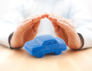 Car insurance concept with blue car toy covered by hands