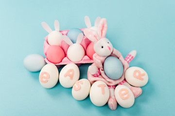 Painted chicken eggs with easter lettering and decorative bunnies on blue background