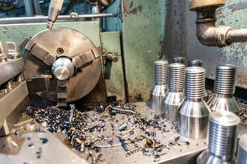 Bolt threading on a lathe in a machine shop, finished products on a machine bed.