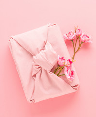 Holiday gift wrapped in cloth in the style of Furoshiki on a pink background. Zero Waste Life Holiday Concept.
