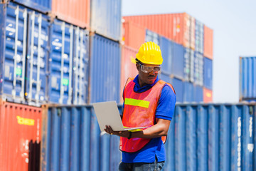 Worker man in hardhat and safety vest holding laptop, Foreman control loading containers box from cargo