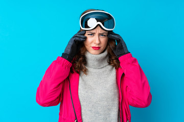 Skier woman with snowboarding glasses over isolated blue wall unhappy and frustrated with something. Negative facial expression
