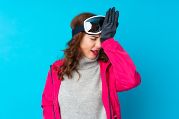 Skier woman with snowboarding glasses over isolated blue wall having doubts with confuse face expression