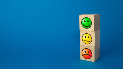 three wooden cubes with different emotions stand on a blue background