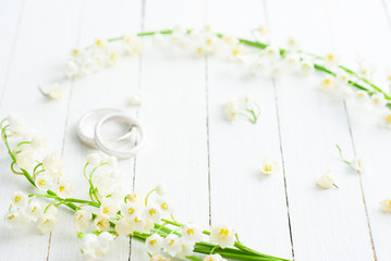Lily of the valley with wedding rings on white wooden