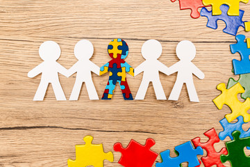 Top view of special kid with autism among another and pieces of multicolored puzzle on wooden background - obrazy, fototapety, plakaty