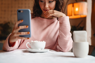Woman indoors in cafe drinking coffee using mobile phone.
