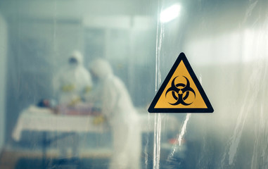 Unrecognizable doctors with bacteriological protection suits attending a patient infected with a...