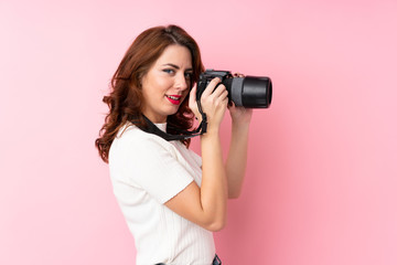 Young Russian woman over isolated pink background with a professional camera