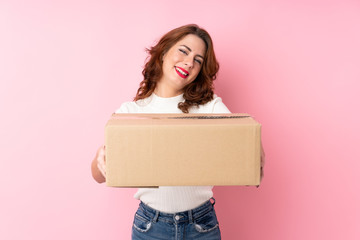 Young Russian woman over isolated pink background holding a box to move it to another site