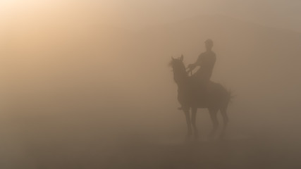 Unidentified man riding a horse in dust and fog