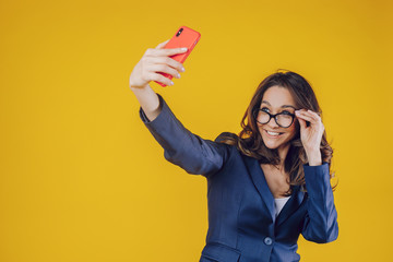 The elegantly dressed European woman raises her hand holding the phone to make a selfie, feels...