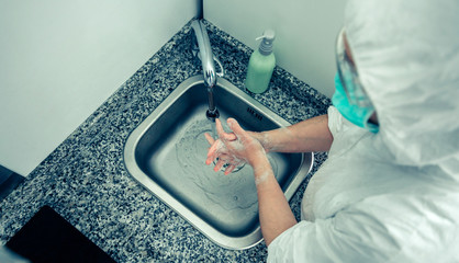 Top view of unrecognizable woman in bacteriological protection suit washing her hands with soap