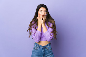 Young brunette woman over isolated purple background nervous and scared putting hands to mouth