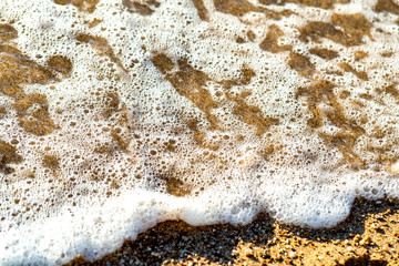 Close up of small sea waves with clear blue water over yellow sand beach at summer sunny shore.