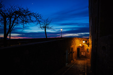 A small road among the old houses of a medieval village in the province of  Italy in beautiful sunset. View through archway of beautiful building and street lamp in  Italy in early evening light.