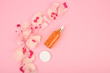 Obraz na płótnie Canvas Cosmetic bottle with natural serum on pink desk. Branding mock up and copy space. Roses essence