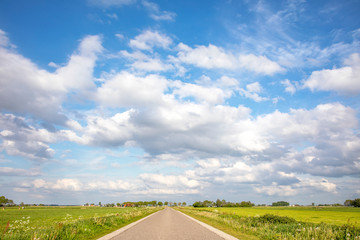 Fototapeta na wymiar Road in Holland countryside, perspective, cloudy sky and green meadows and a horizon.