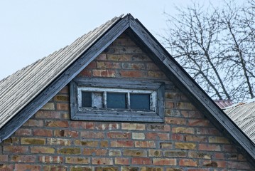 old brown brick loft with a small gray wooden window against a blue sky