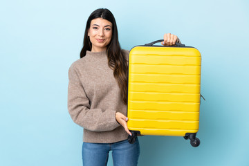 Young brunette girl over isolated blue background in vacation with travel suitcase