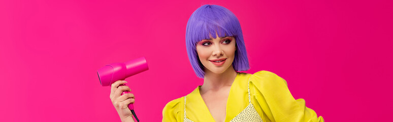panoramic shot of happy pop art girl in purple wig using hair dryer, isolated on pink