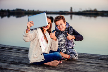 Two young cute little friends, boy and girl having fun playing on digital tablet outdoor