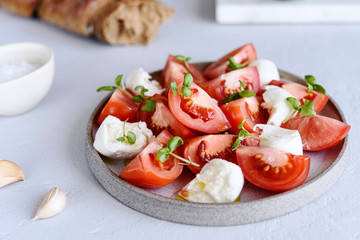 Italian Сaprese salad with sliced tomatoes, mozzarella cheese, basil, olive oil in a plate on grey concrete table. Selective focus