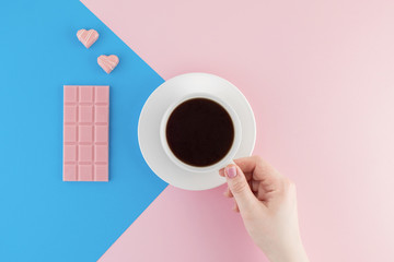 Female hand holds a cup of freshly brewed coffee on beautiful pink and bright blue pastel background.