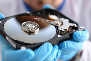 Obraz premium A male repairman wearing blue gloves is holding a hard drive from computer or laptop in hands. Performs fault diagnostics and performs urgent repairs recovery of lost data during deletion HDD closeup