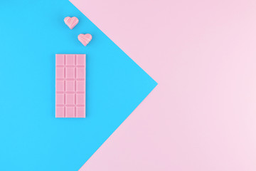 Pink chocolate and heart shaped candies on beautiful pink and bright blue pastel background.