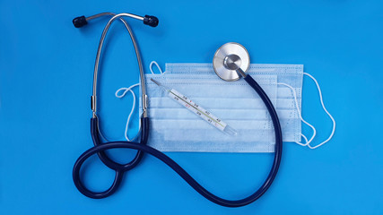 Thermometer with temperature stethoscope and medical mask on a blue background