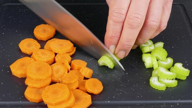 cutting celery stalk into slices on a black cutting board with a kitchen knife closeup 4k
