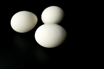 Three white chicken eggs on a black background