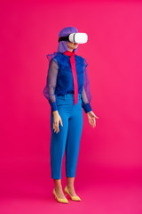 attractive pop art girl in blue fashionable blouse using virtual reality headset, on pink