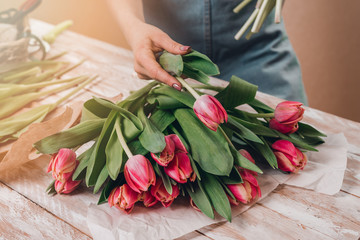 Hands of young woman florist working with fresh flowers making bouquet of pink roses on table.
