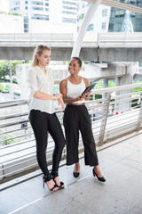 Obraz premium Businesswoman Showing Digital Tablet To Female Colleague On Walkway Bridge In City