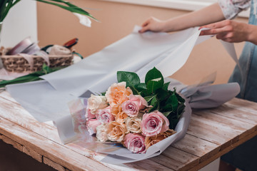 Hands of young woman florist working with fresh flowers making bouquet of pink roses on table.