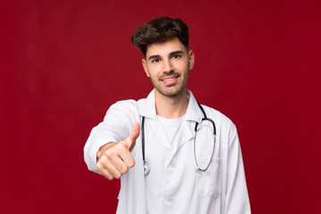 Young man over isolated background with doctor gown and with thumb up
