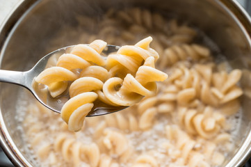 A spoon with whole grain fusilli on a pasta background, cooked in a saucepan. Healthy eating