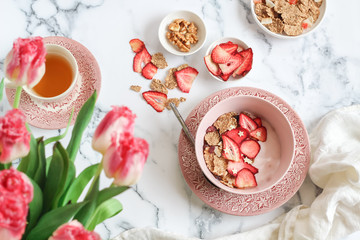 Breakfast scene with yogurt, granola and dried strawberries bowl and a cup of tea on a mable table 