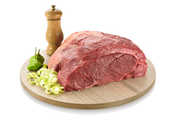 Raw topside beef or part of the round steak, ready to be cooked. On a cutting board with leek and peppers aside, isolated on white background