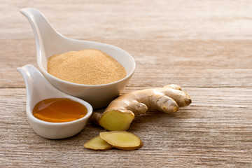Ginger root with slice, ginger powder and honey in white ceramic bowl isolated on wood table background.