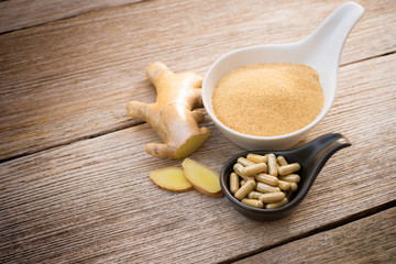 Dried ginger powder with capsule in  cera bowl and fresh ginger root with  slice isolated on wood table background. Supplement concept. Top view. Selective focus.