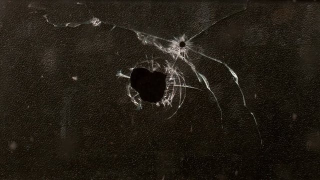 Shot Glass breaking with bullet holes on black background