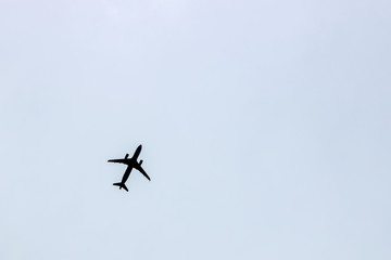 Black silhouette of a flying airplane against a blue gray sky background