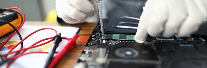 Focus on laptop fixing process. Personal computer repairing by man using screwdriver and wearing protective gloves. PC support technical service for professional gadgets restoring